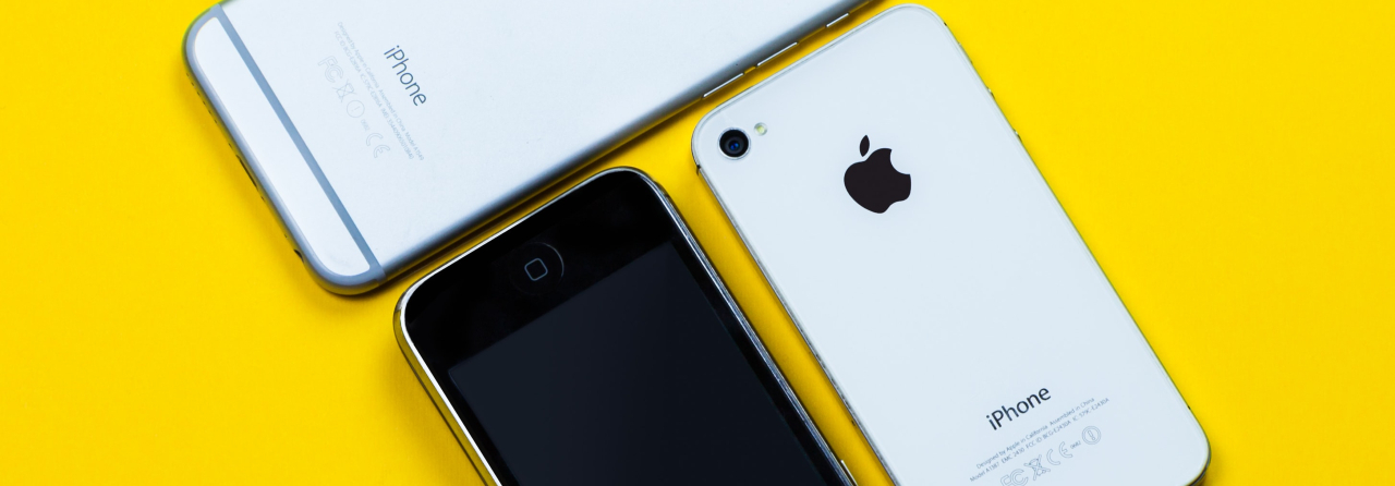 Three Apple Iphones laid down on a yellow surface