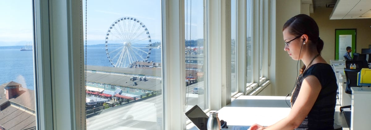 Young woman working on a laptop with earphones in next to a view of a ferris wheel
