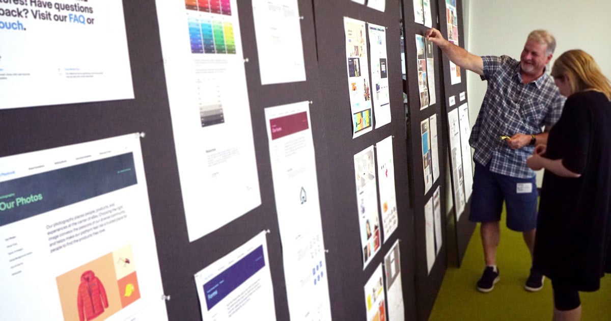 Two clients review the design audit posted on giant black posters around the room.