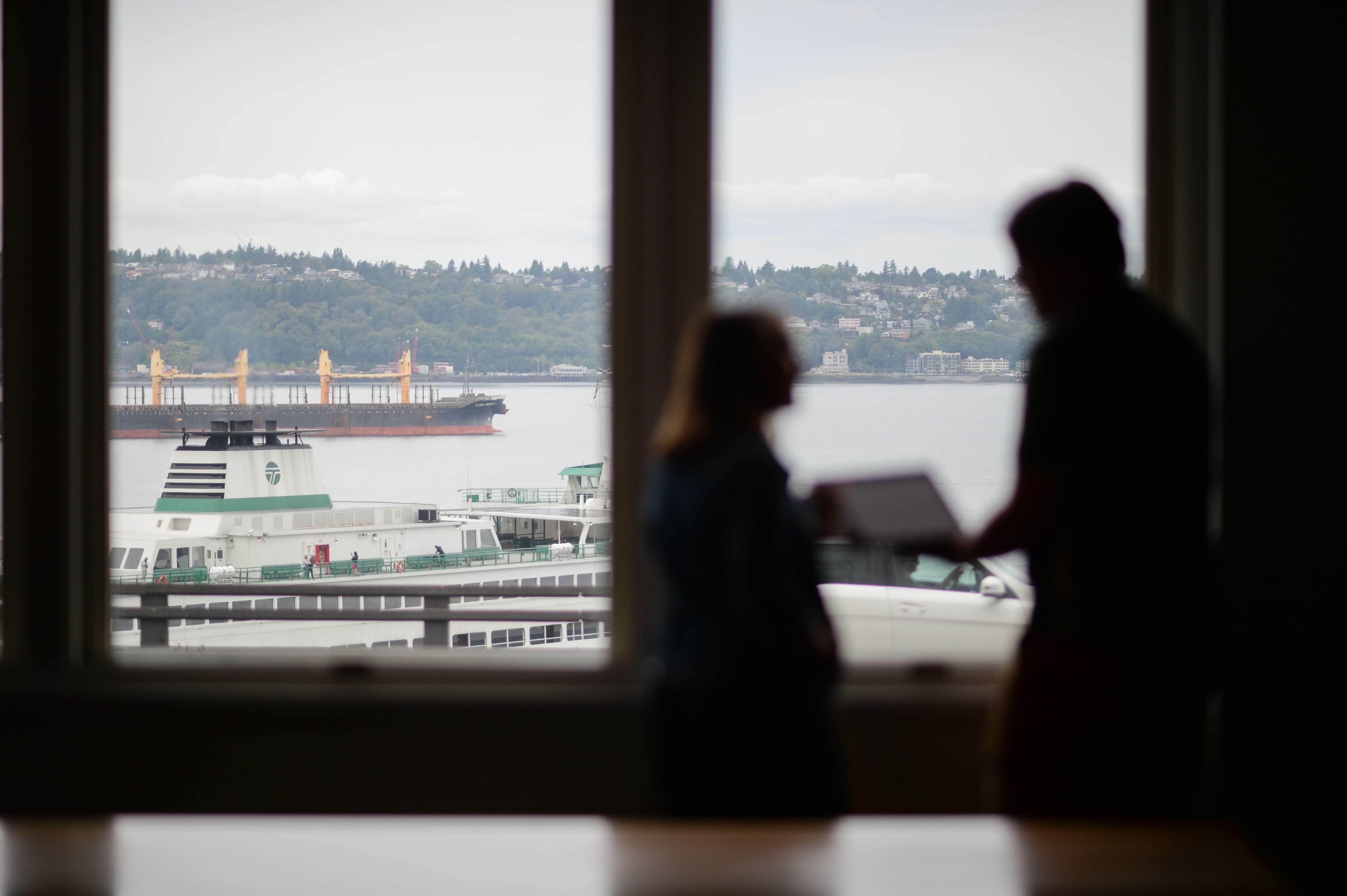 Two coworkers having a discussion in front of a window with a ferry boat in the background