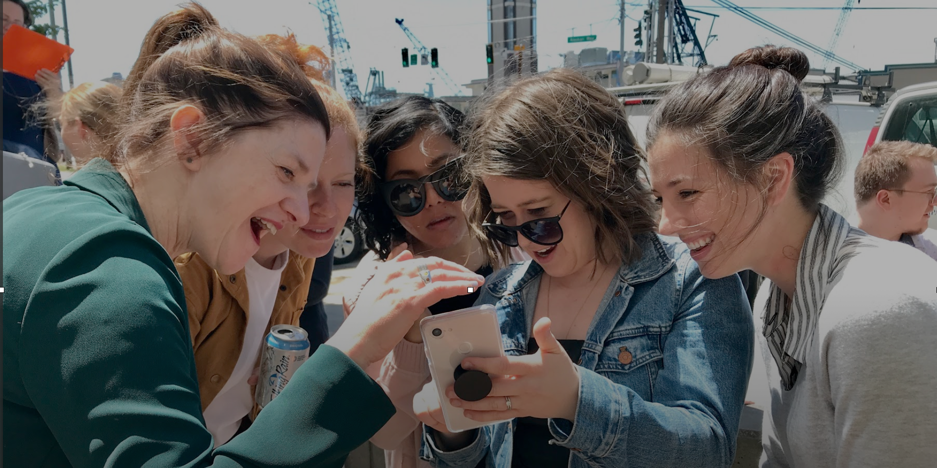 Group of people huddling over a phone looking at the screen and laughing.