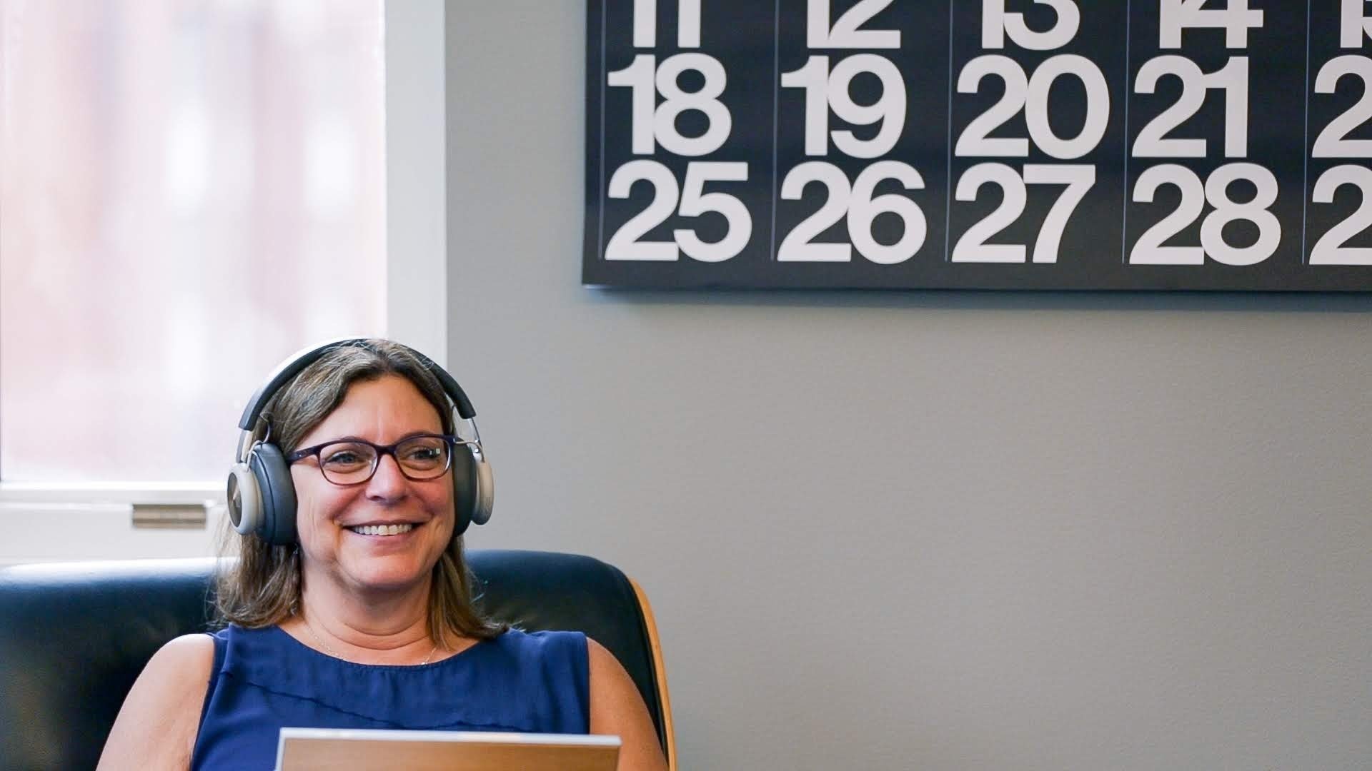 Director of Client Relations, Anne, sitting in a chair our Seattle studio while wearing headphones and looking at an Ipad.