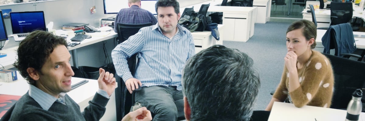 Man gesturing with his hands as he talks to three coworkers.