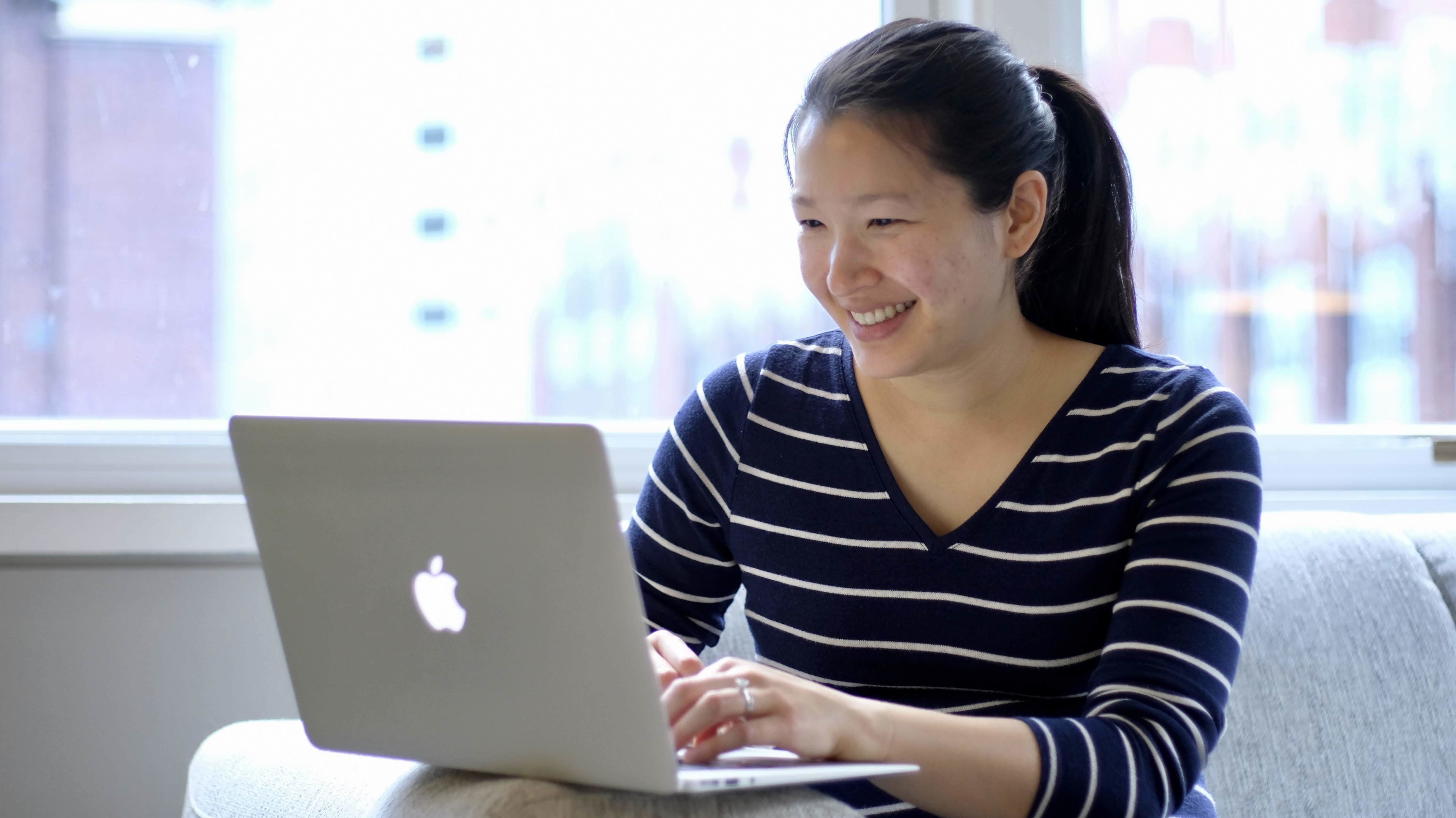 Woman smiling at an Apple laptop.