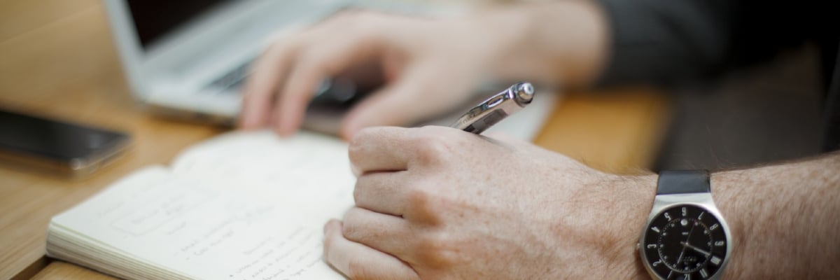 Close-up of a person wearing a watch taking notes in a notebook.