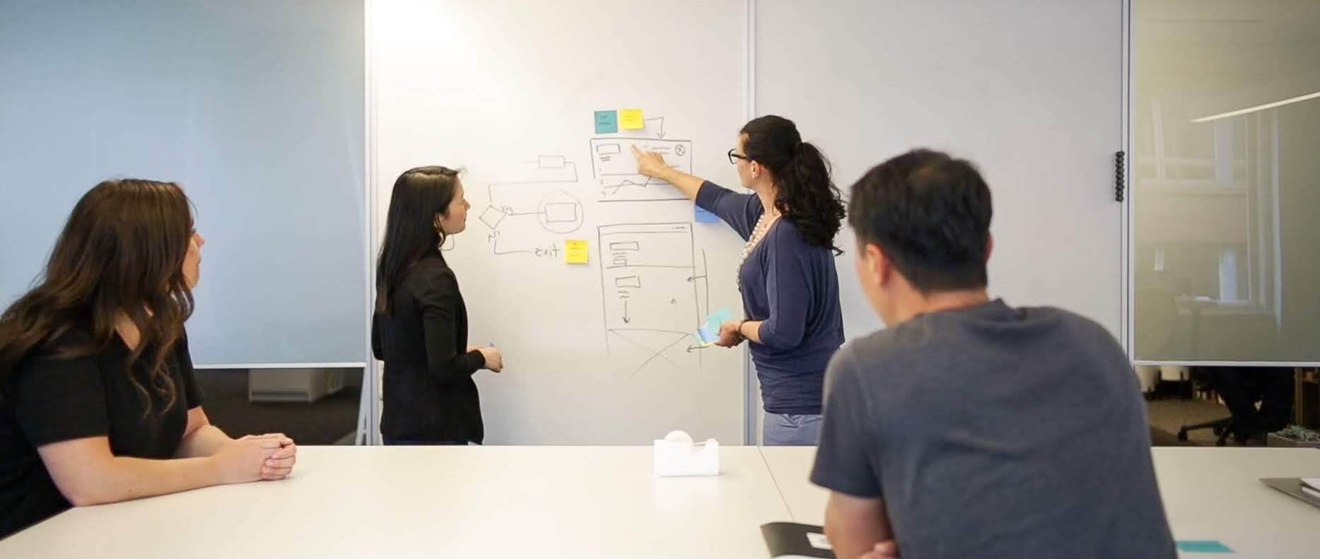 UX professionals discussing a diagram drawn on a whiteboard.
