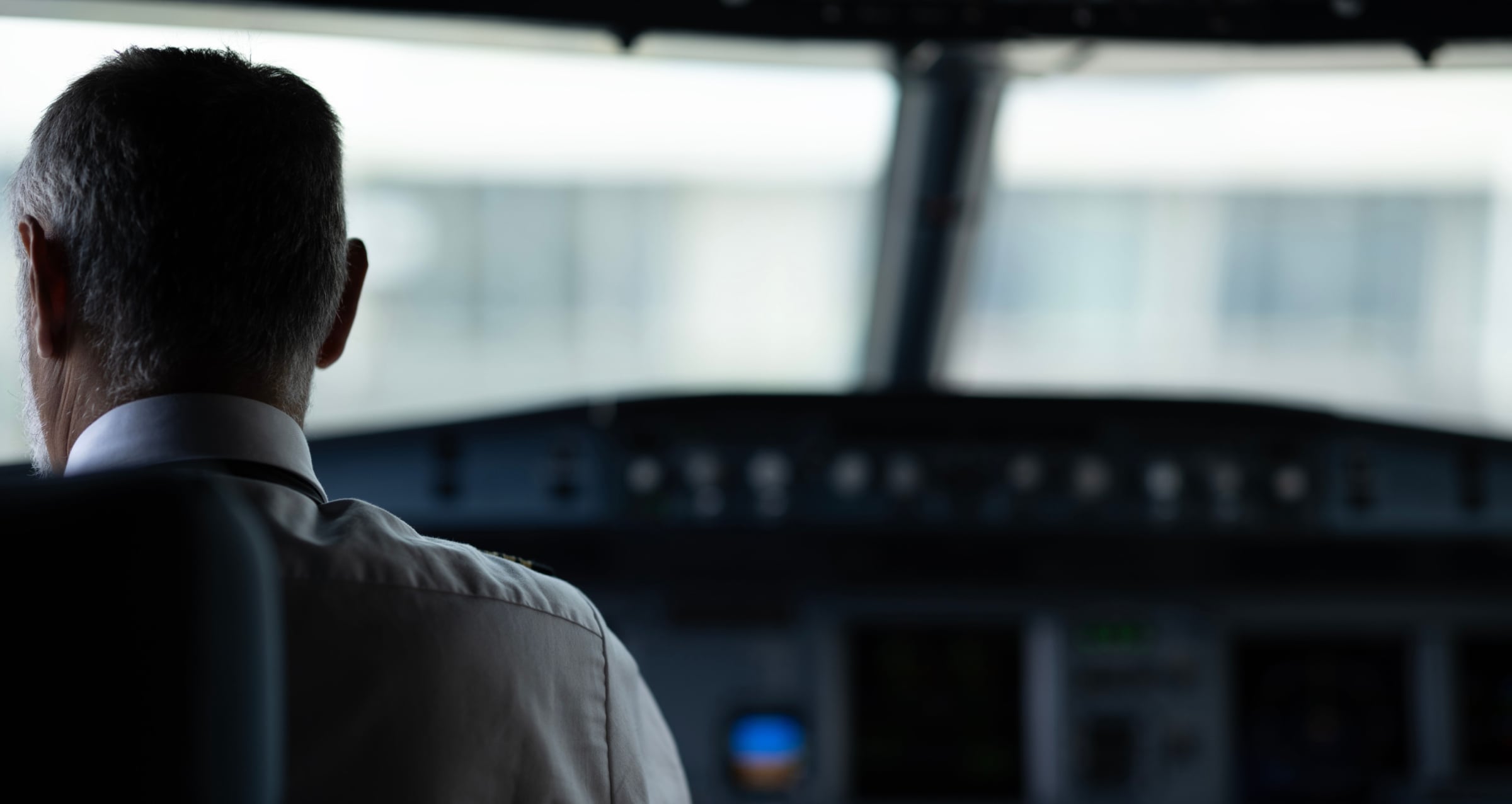 Pilot from behind his seat in front of a airplane cockpit controls