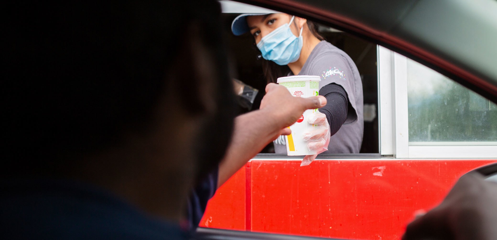 Drive-thru worker with a mask on handing a drink to a customer.