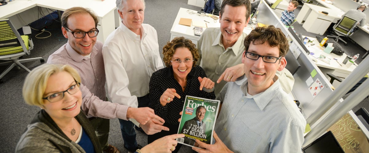 Group of Blink team members pointing towards copy of Forbes magazine.