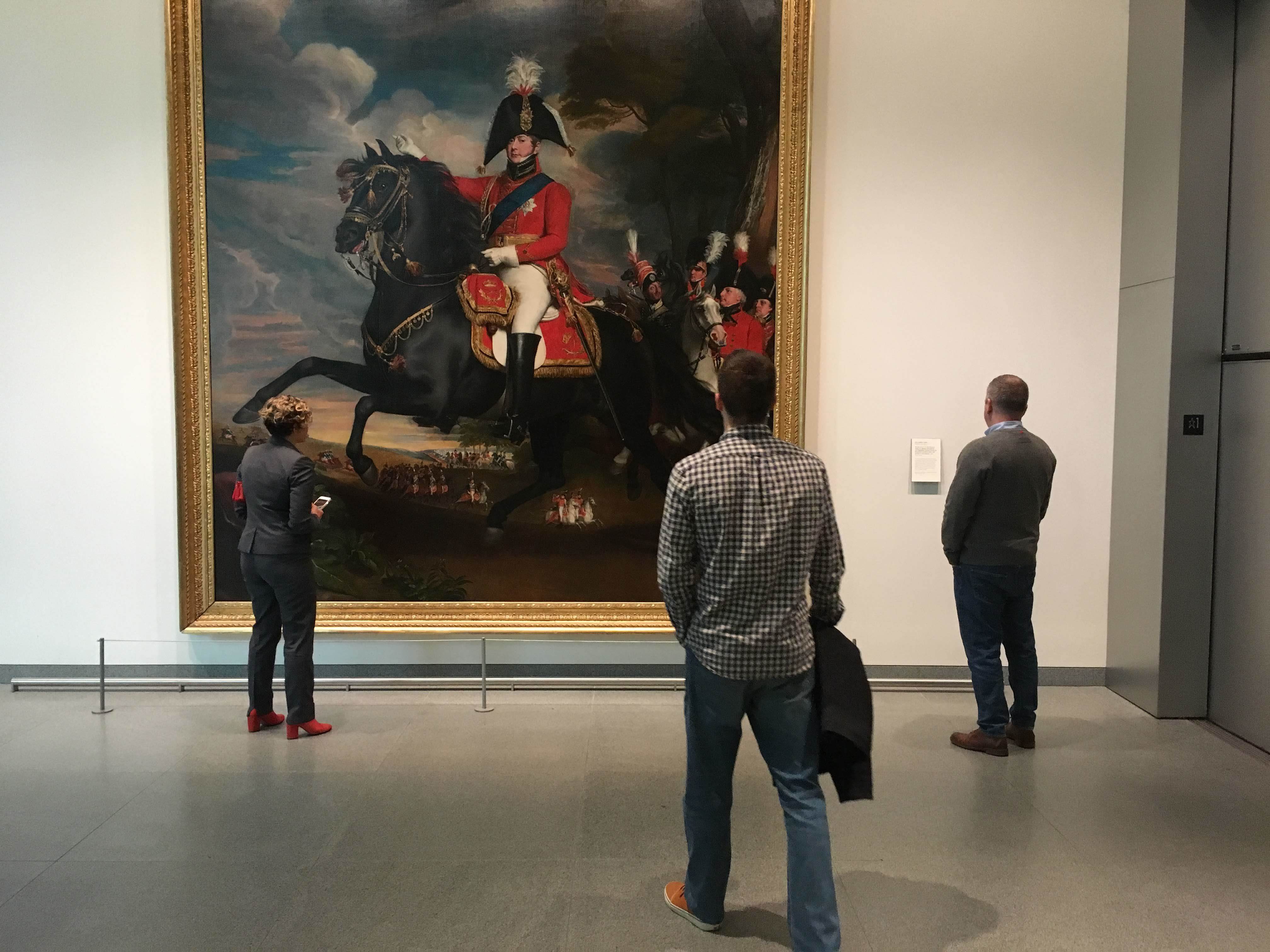 Three people admiring a large painting in an art gallery.