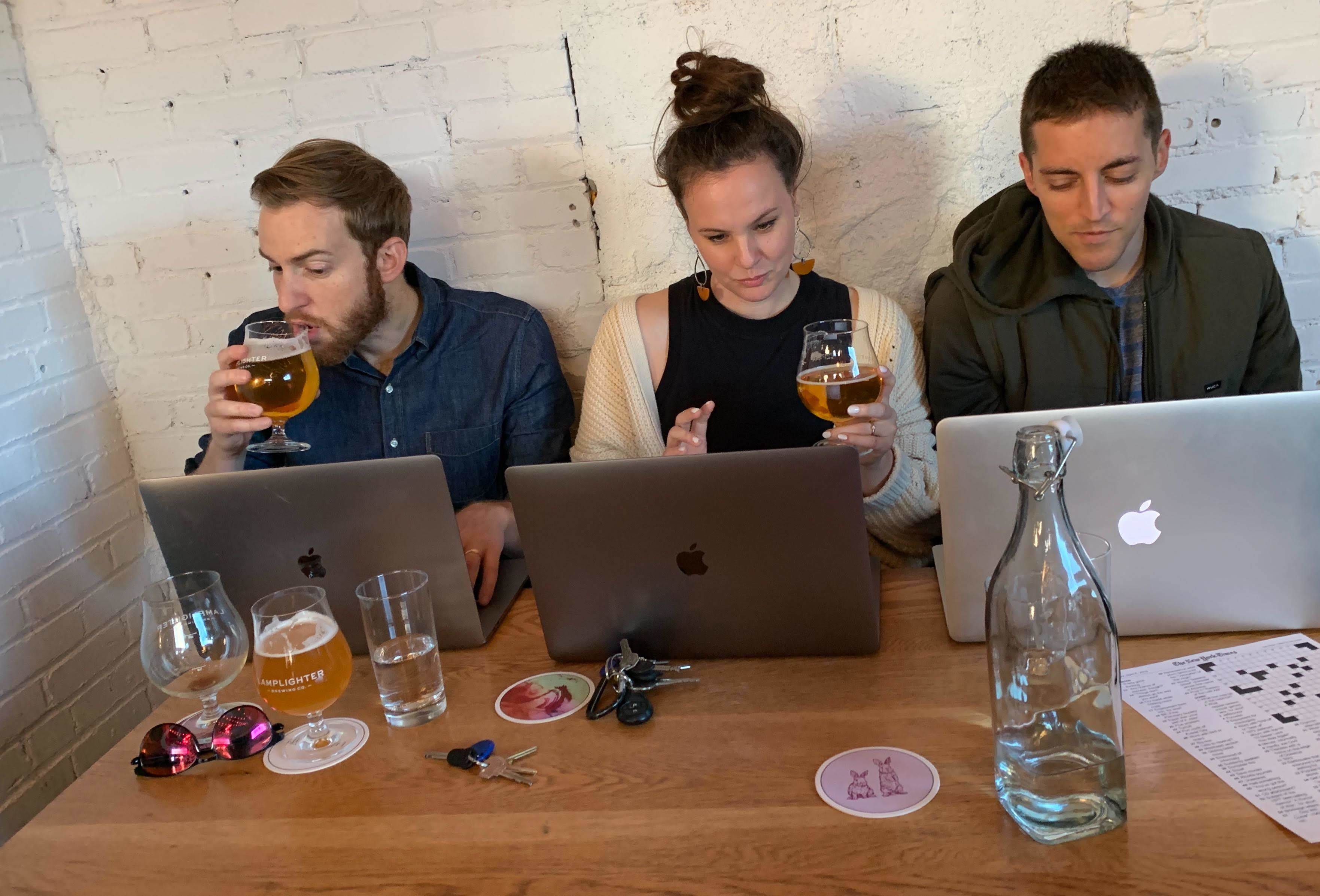 Three people seated at a table working on Apple laptops.